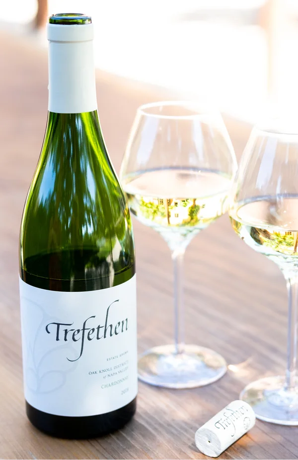 A bottle of Trefethen with two filled glasses on a table in daylight.
