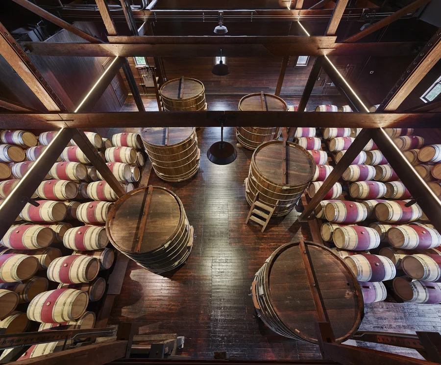 The barrel cellar inside the historic winery: rows of barrels between heavy timber posts and beams.